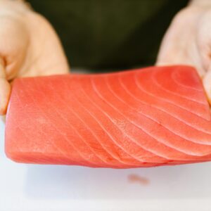 Close-up of hands holding a slice of fresh, raw salmon, ideal for sushi or sashimi preparation.