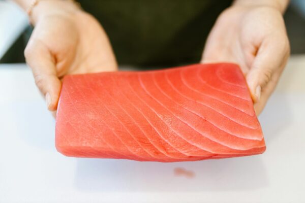 Close-up of hands holding a slice of fresh, raw salmon, ideal for sushi or sashimi preparation.