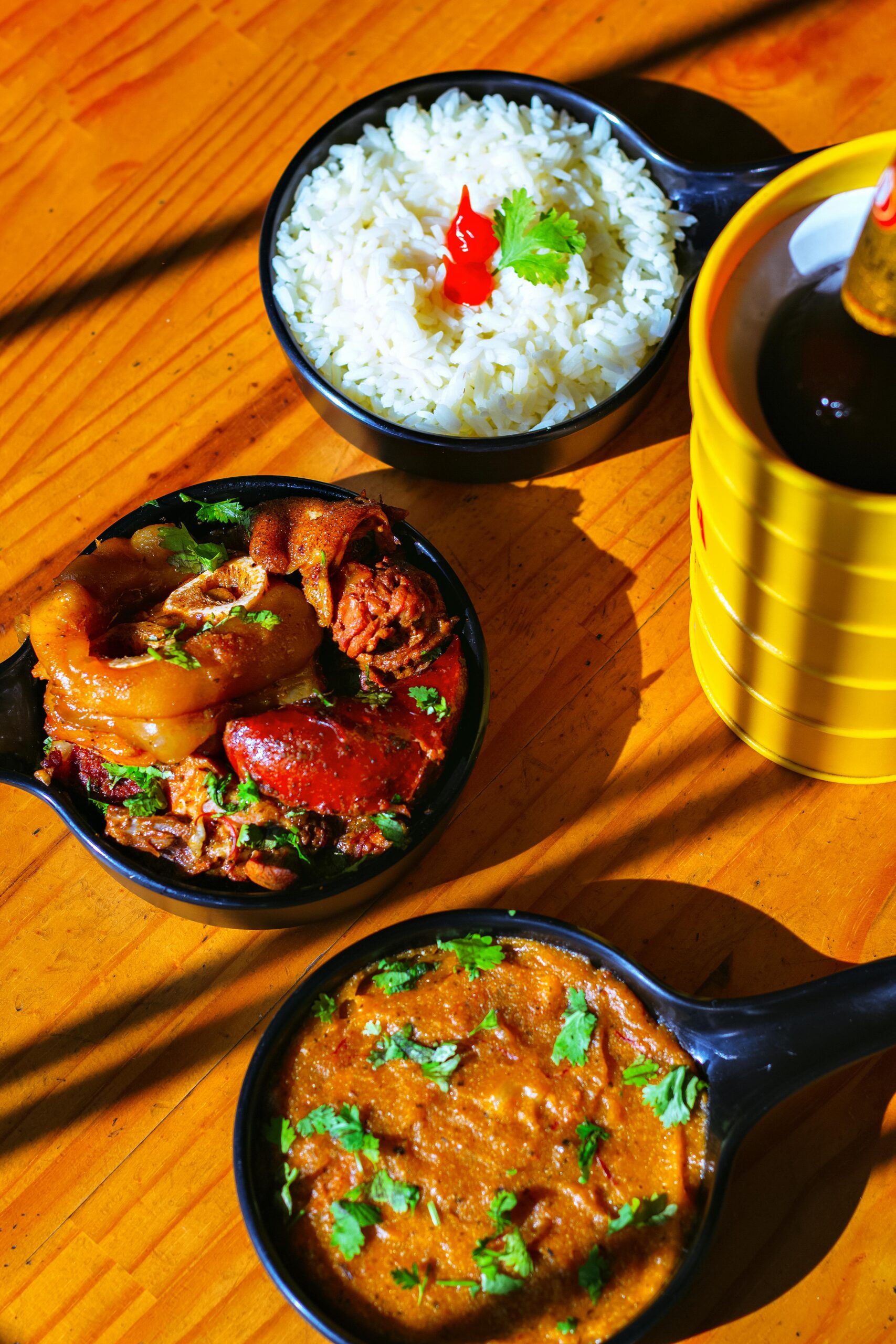 Delicious Indian dishes with rice and curry served in black bowls on a wooden table.