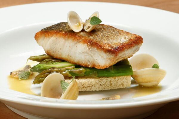 A gourmet fish dish served with clams and asparagus on a white plate.
