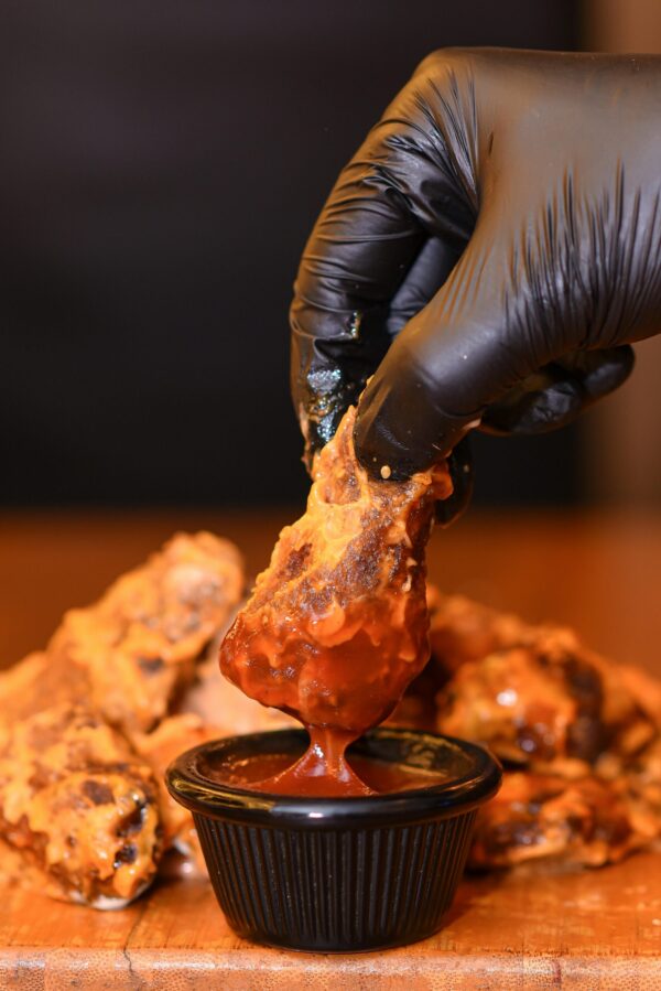Close-up of crispy chicken wing dipped in hot sauce, perfect for food lovers.