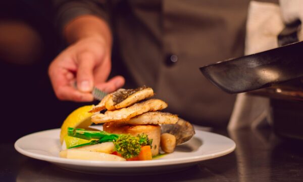 Gourmet fish dish with vegetables being served by a chef in a UK restaurant.