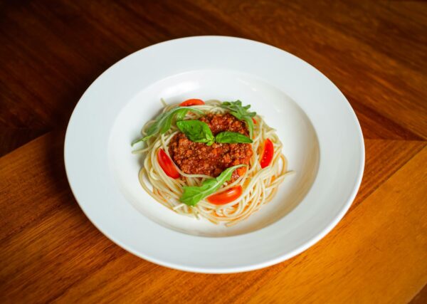 A close-up of a flavorful spaghetti bolognese garnished with basil leaves and cherry tomatoes on a stylish dining table.