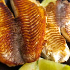 Delicious grilled tilapia fillets served with fresh lime wedges on a dark plate.