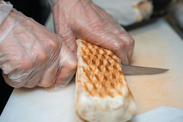 Close-up of hands slicing shawarma with a knife on a cutting board.