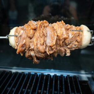 Close-up of raw chicken shawarma being grilled on a skewer, ready for cooking.
