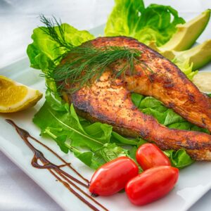 Delicious grilled salmon served with fresh vegetables and herbs on a white plate.